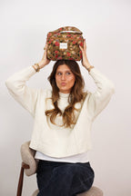 Woman balancing the large mustard and red floral jacquard squared toiletry bag on her head to show its size