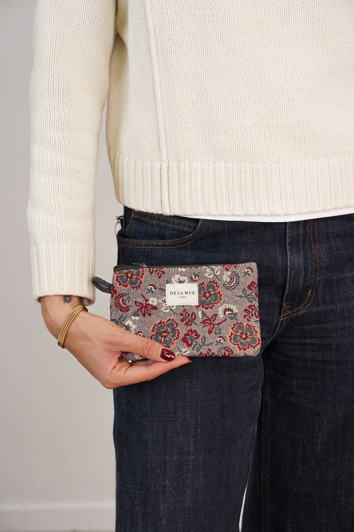 Burgundy and gray floral jacquard small pouch and coin purse held by a woman in a cream sweater and jeans, shown for size