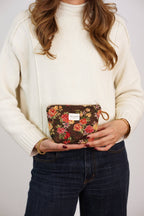 Dark brown and red floral jacquard small makeup bag held by a woman in a cream sweater and jeans, shown for size