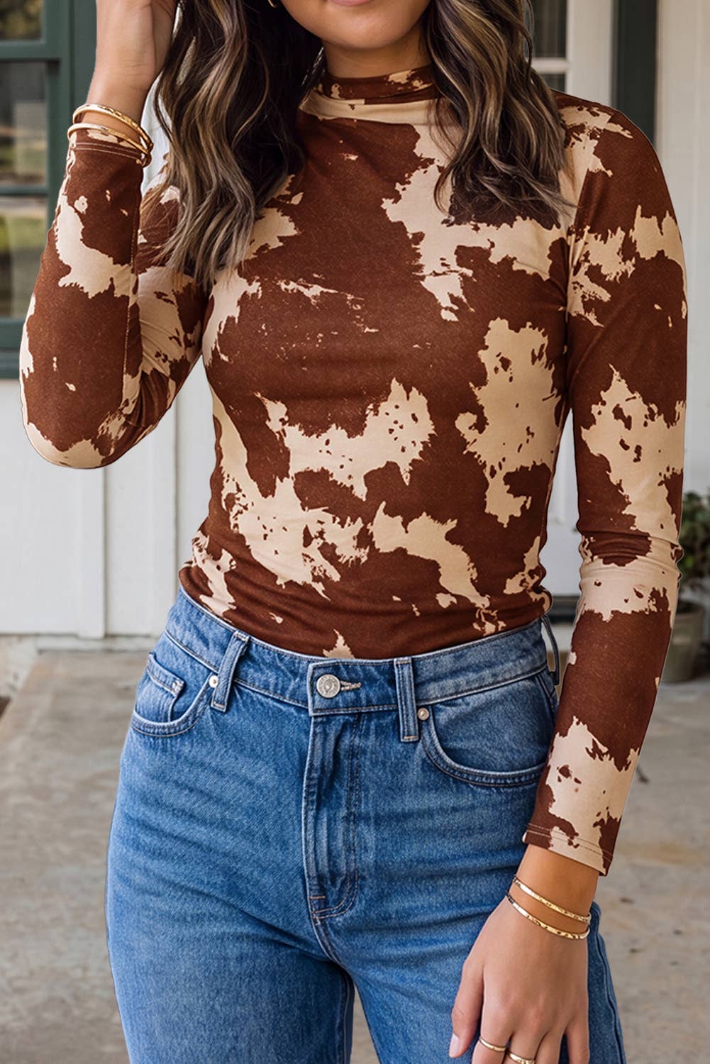 A woman posing in a mockneck top with brown and beige cow print, paired with blue jeans.