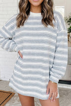 A woman wearing a long-sleeve crewneck sweatshirt dress with horizontal gray and white stripes, standing in an outdoor setting.