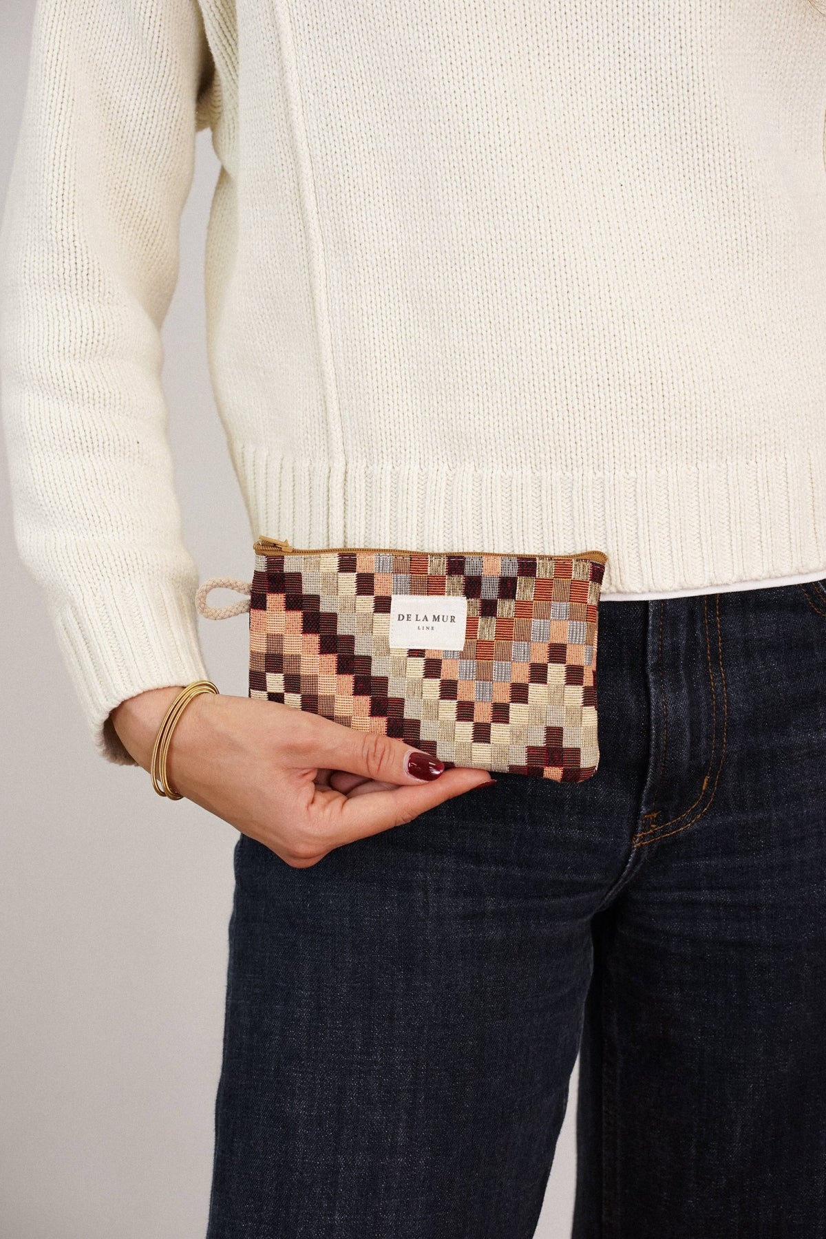 Brown and beige zigzag jacquard small pouch and coin purse held by a woman in a cream sweater and jeans, shown for size