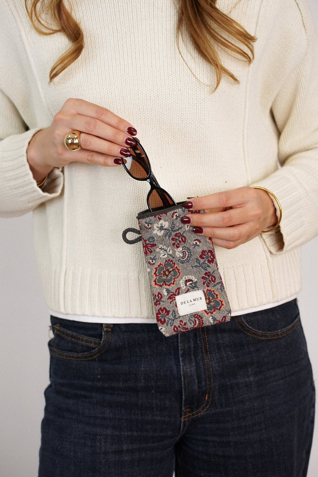 Burgundy and gray floral jacquard glasses case held by a woman in a cream sweater and jeans, shown for size