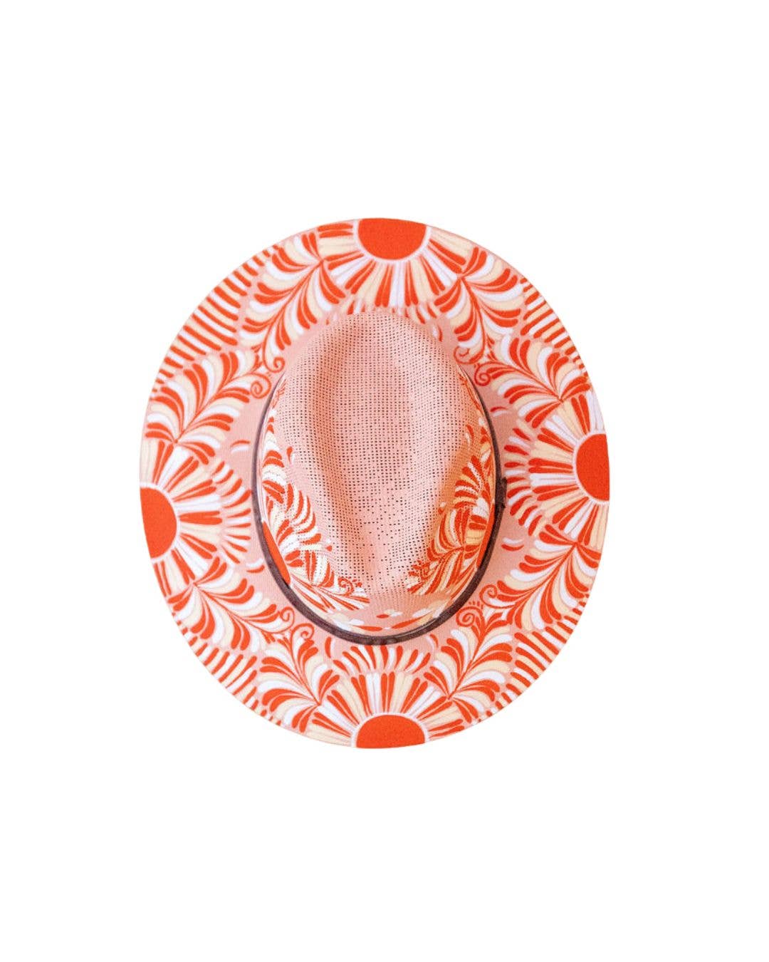 A top-down view of a fedora hat featuring an artisan painted vibrant orange and white sunburst pattern on the brim and a textured light pink crown. Crafted in Oaxaca, Mexico.