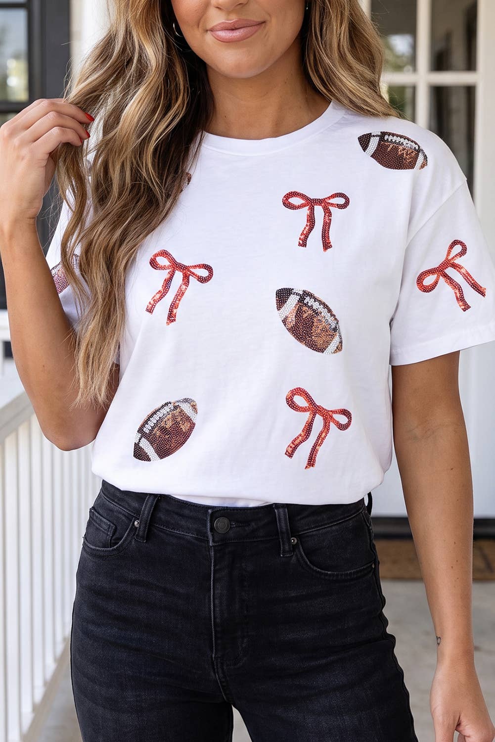 A woman wearing a white short-sleeve t-shirt with a pattern of red ribbon bows and footballs, paired with black jeans.