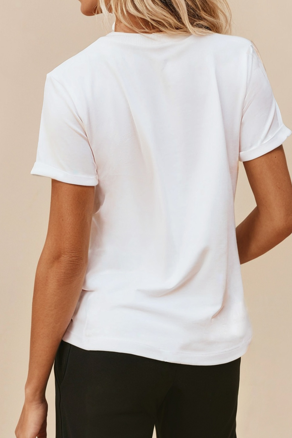 A woman viewed from the back wearing a plain white short-sleeve crewneck T-shirt and black pants, set against a solid beige background.