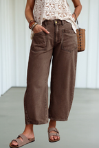 A person wearing loose, wide-leg cropped brown pants with a cream crochet top, brown sandals, and a small brown woven bag, standing indoors against a light neutral wall.