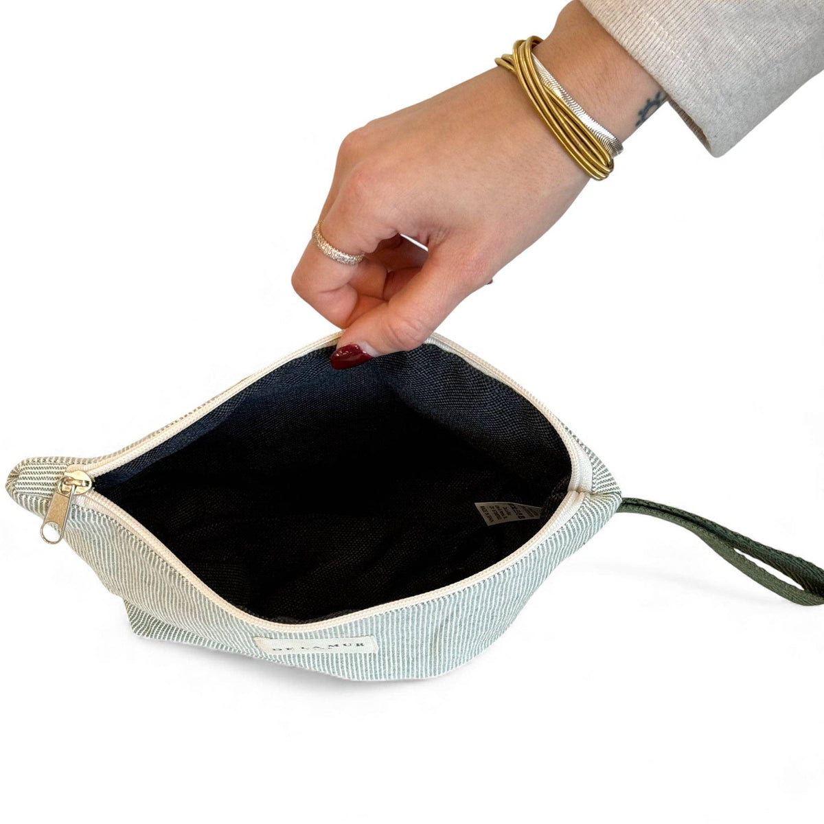 Hand unzipping the large sage green and cream striped makeup bag to show the dark lining