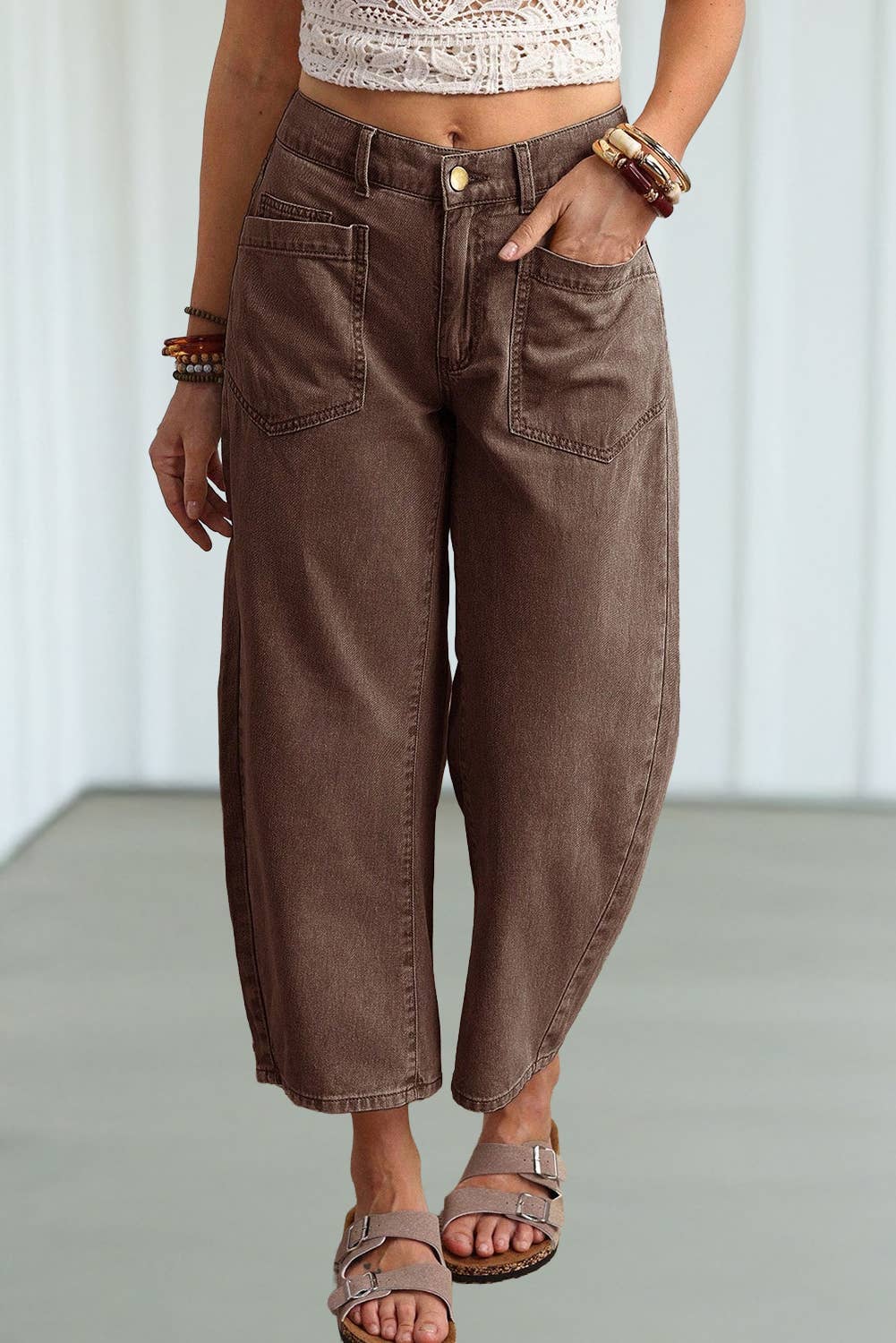 A person wearing brown wide-leg cropped jeans with a relaxed, baggy fit, paired with a cream crochet top and brown sandals.