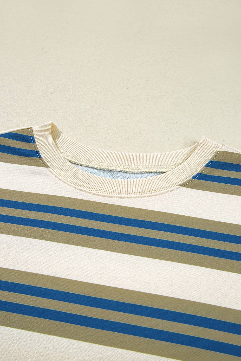 Close-up of a striped crewneck shirt with horizontal beige, white, and blue stripes, featuring a ribbed cream collar.