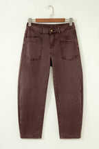 A pair of dark brown washed denim jeans hanging on a wooden hanger against a plain white wall.