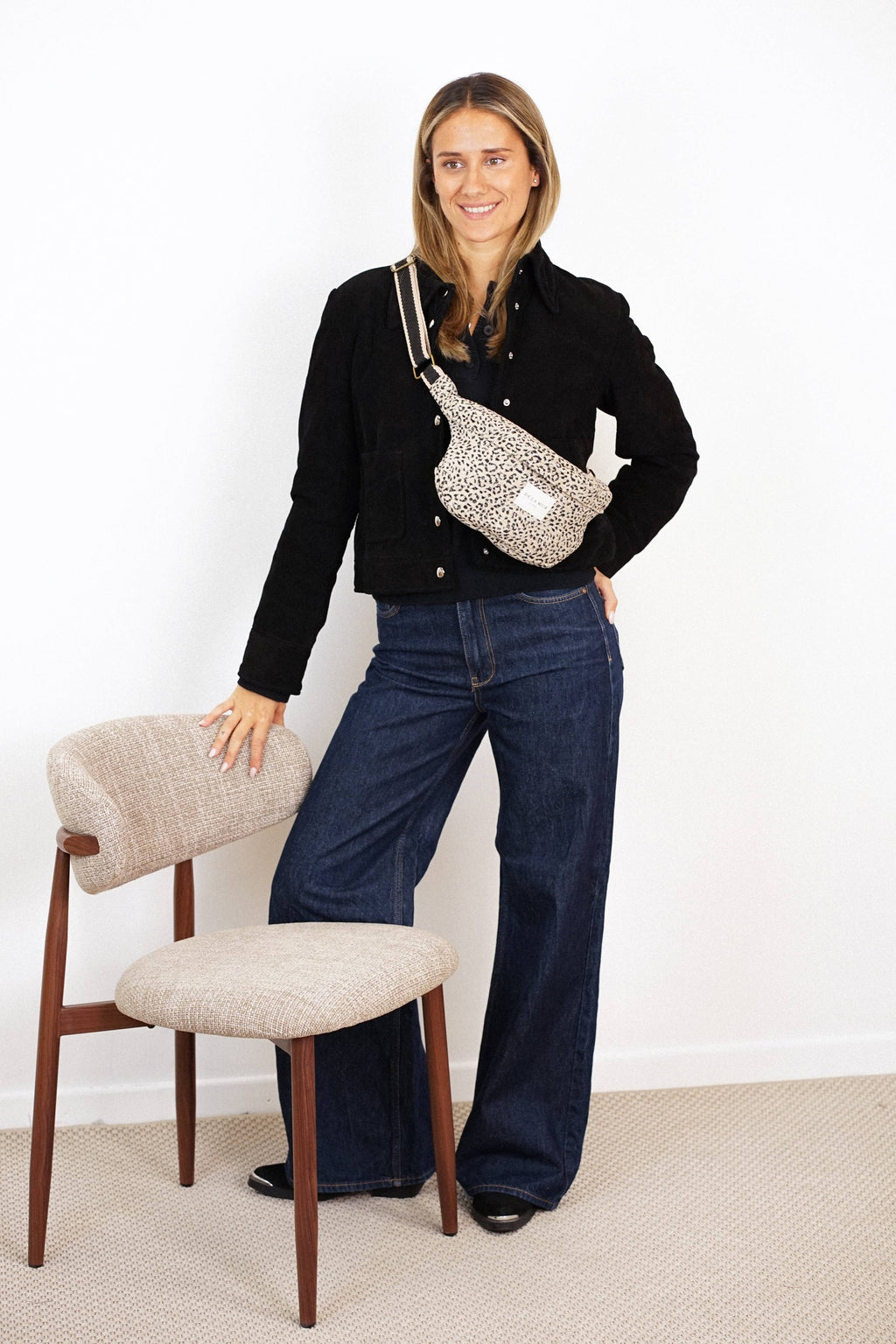 Woman in a black jacket and jeans wearing the beige and black leopard jacquard fanny pack crossbody