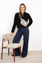 Woman in a black jacket and jeans wearing the beige and black leopard jacquard fanny pack crossbody