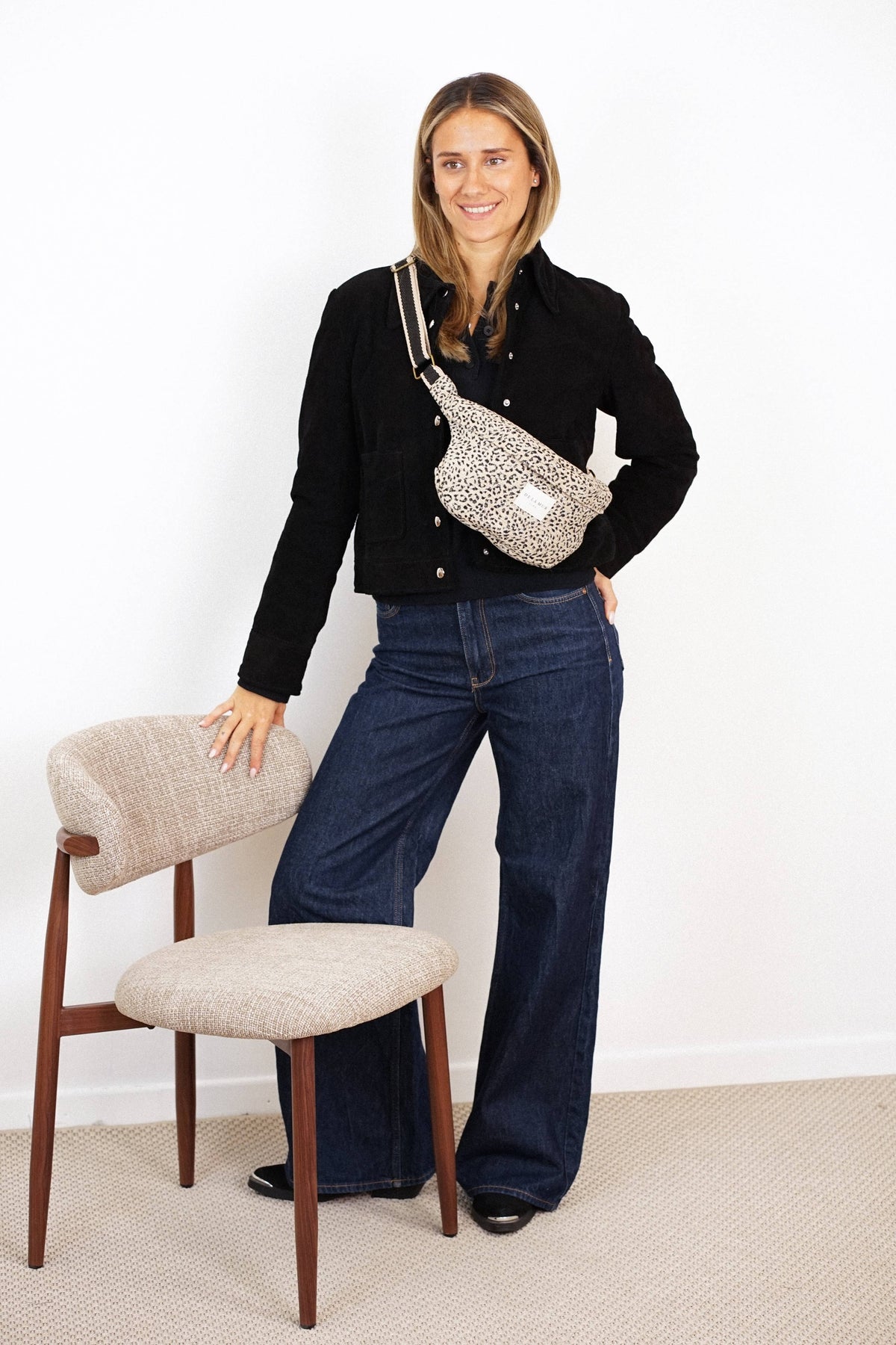 Woman in a black jacket and jeans wearing the beige and black leopard jacquard fanny pack crossbody