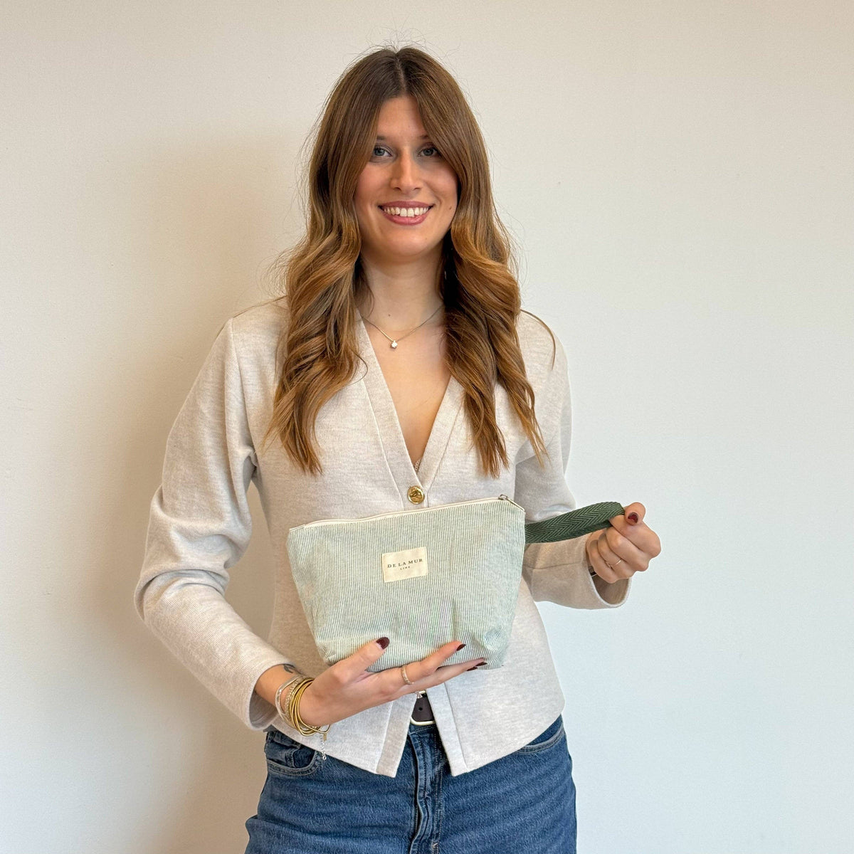 Smiling woman holding the large sage green and cream striped makeup bag, shown for size