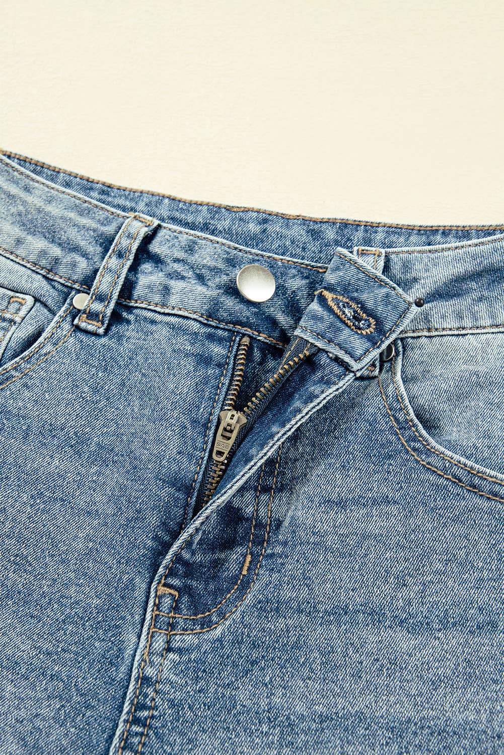 Close-up of blue denim jeans with a zipper and button on a beige background