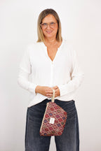 Woman in a white top holding the large burgundy geometric jacquard makeup bag, shown for size