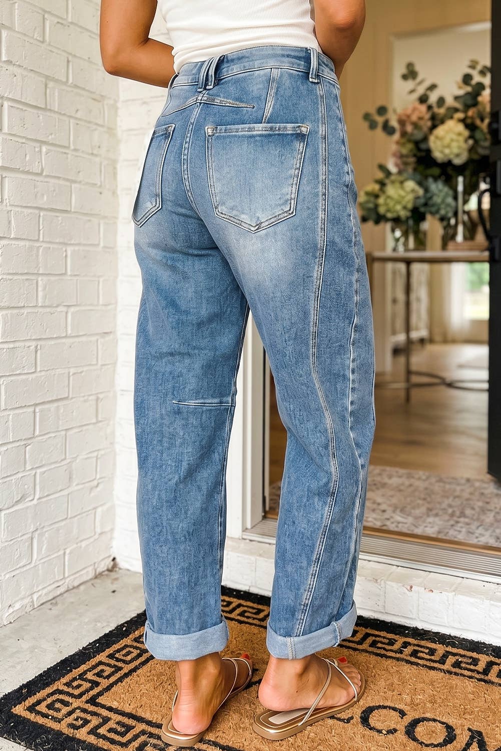 A person wearing light blue wide-leg cropped jeans with rolled cuffs and back pocket details, standing indoors near a white brick wall and doorway.