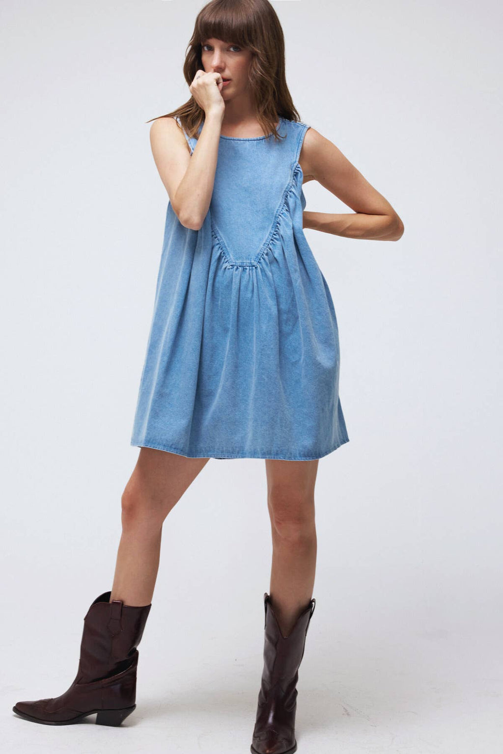 Woman wearing a light blue dress with brown cowboy boots on a white background