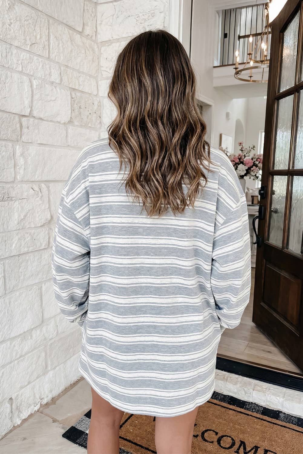 A woman wearing a long-sleeve crewneck sweatshirt dress with horizontal gray and white stripes, standing in a brightly lit setting.