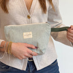 Close-up of hands holding the large sage green and cream striped makeup bag by its cord handle