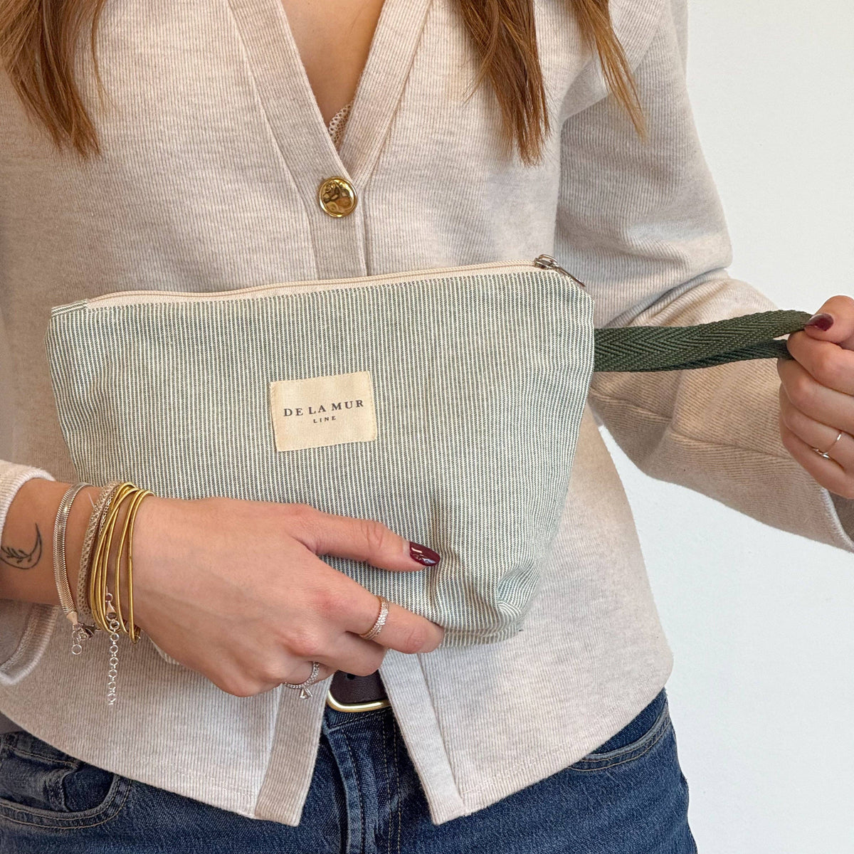 Close-up of hands holding the large sage green and cream striped makeup bag by its cord handle