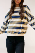 A woman wearing a loose-fit crewneck sweatshirt with horizontal stripes in navy blue, olive green, and cream, paired with black jeans.
