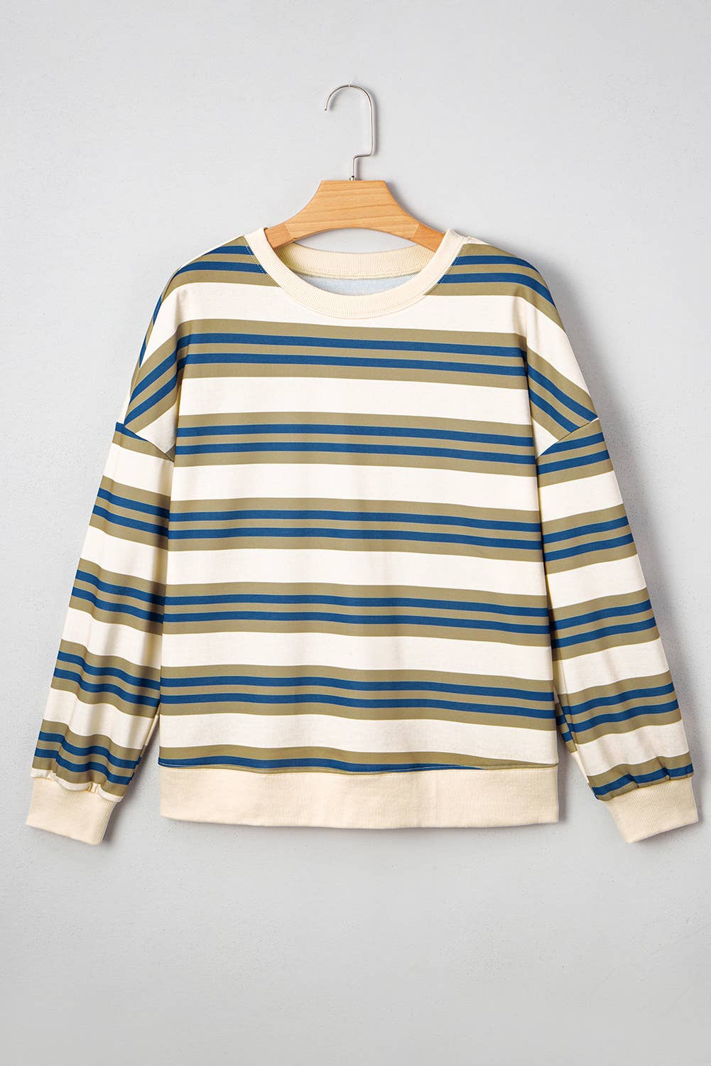 A long-sleeve crewneck sweatshirt with horizontal stripes in blue, olive green, and cream, hanging on a wooden hanger against a light gray background.