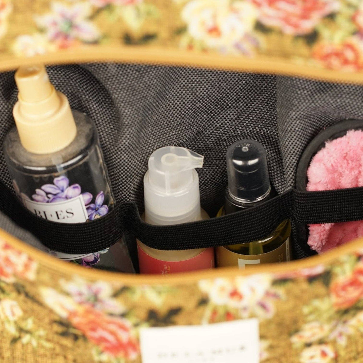 Close-up of the elastic loops holding bottles inside the large mustard and red floral jacquard squared toiletry bag