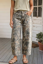 A person wearing wide-leg cropped jeans with a muted camouflage pattern in gray, beige, and brown, paired with a light olive top and tan sandals on a porch.