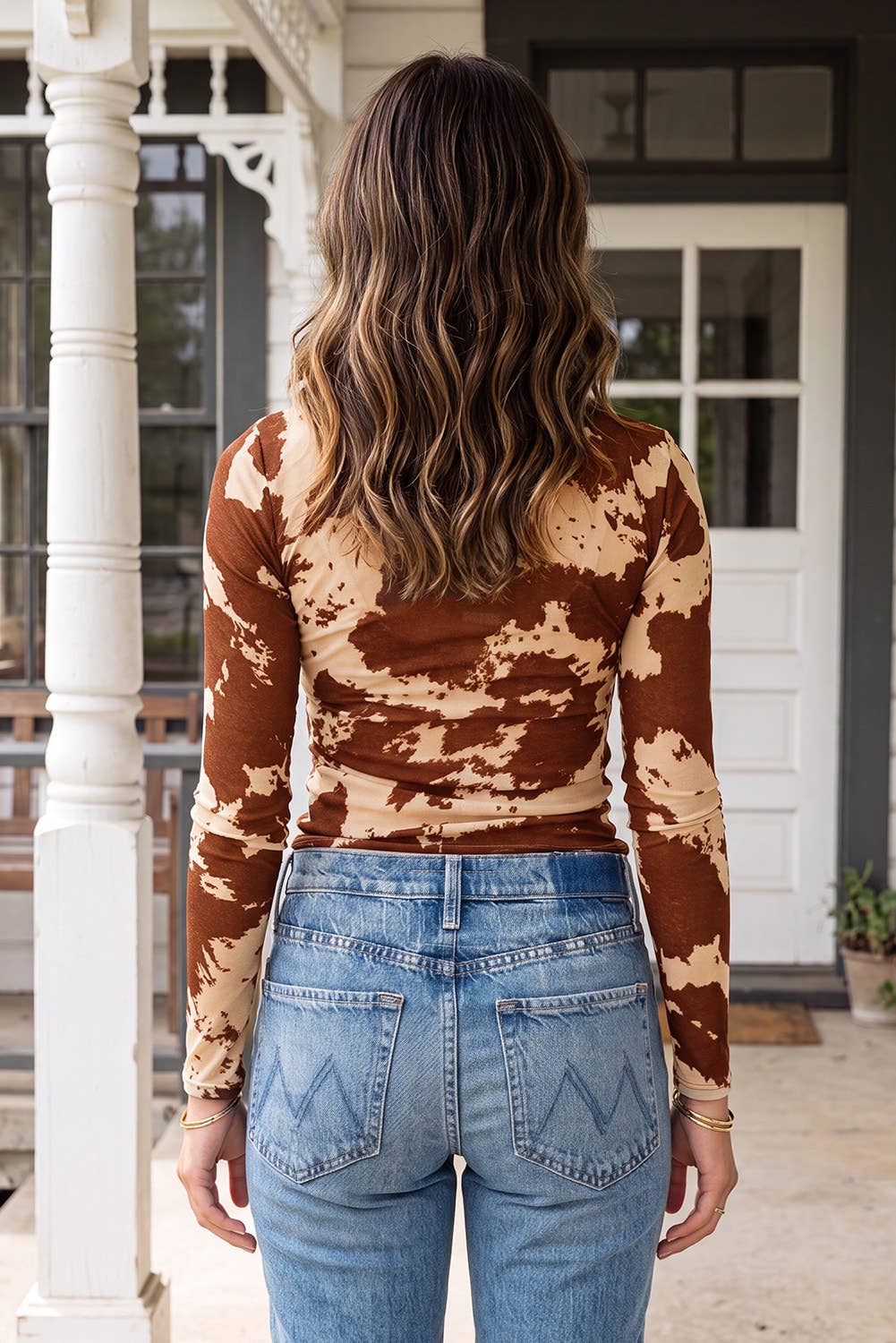 A woman posing in a mockneck top with brown and beige cow print, paired with blue jeans.