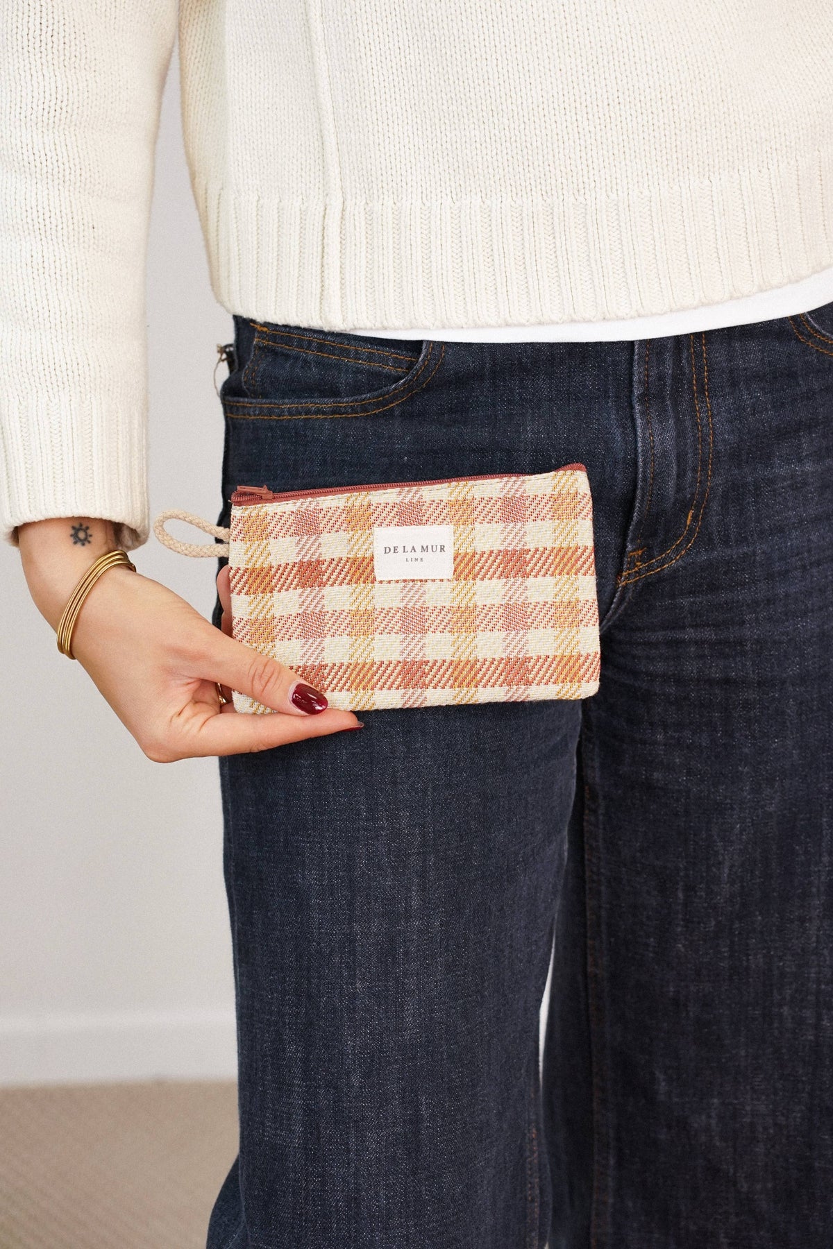 Terracotta and mustard gingham jacquard small pouch and coin purse held at a woman's hip, shown for size